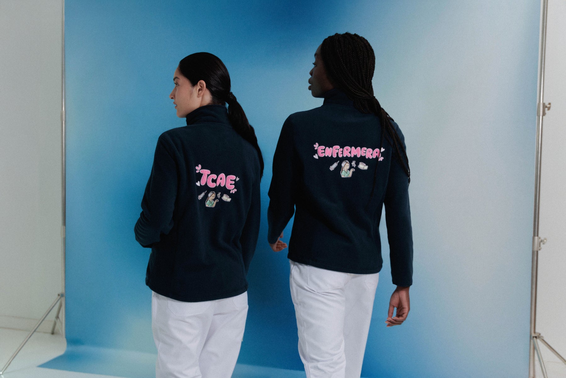 Two nurses wearing the original navy Daily Shift fleece jackets with pink Enfermera and TCAE embroidery